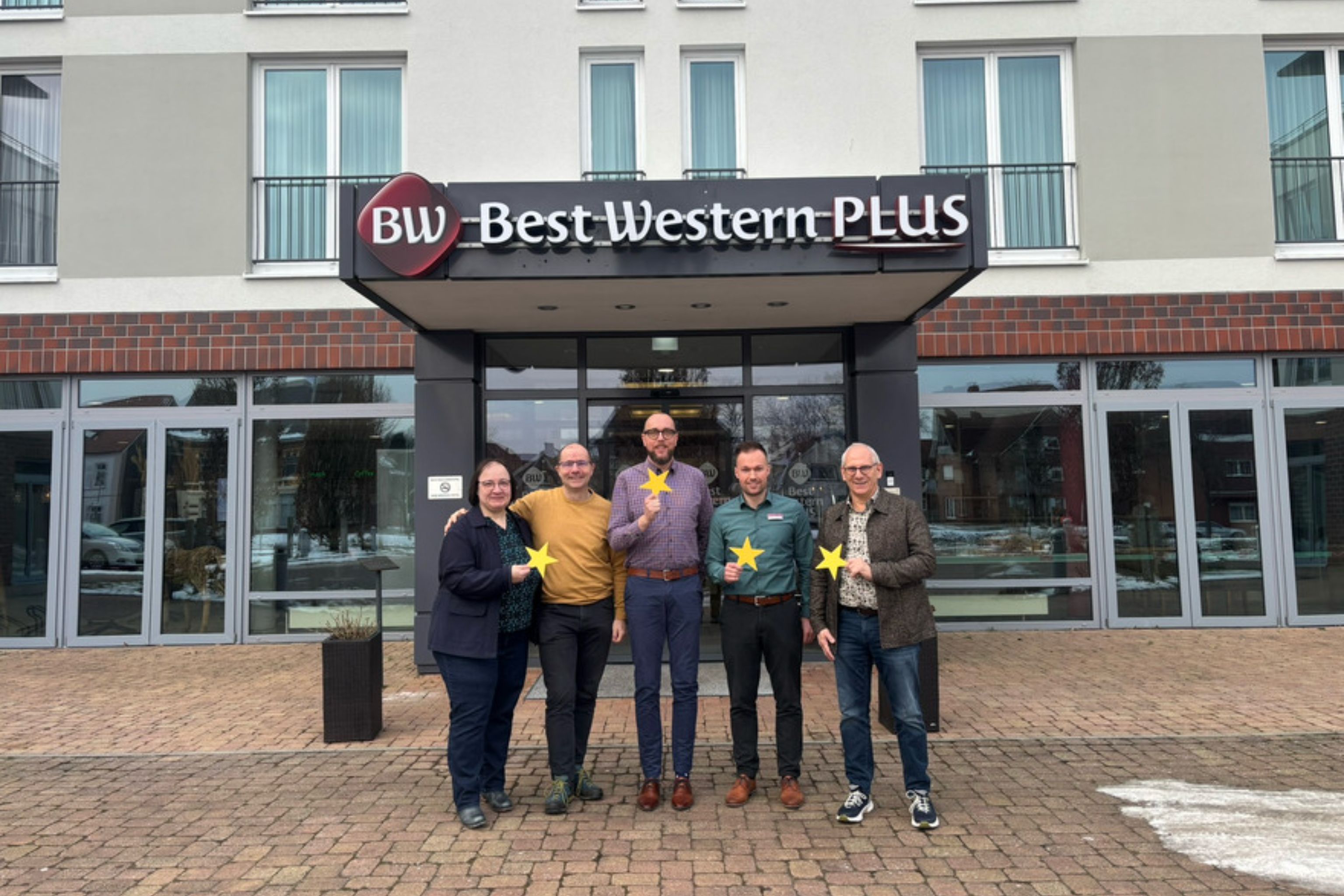 5 Menschen stehen vor dem Best Western Plus Hotel Papenburg und halten gelbe Sterne