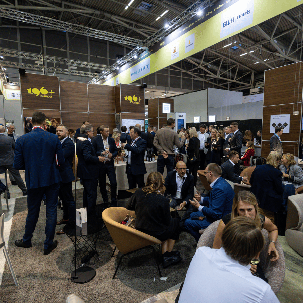Besucher:innen im Gespräch auf einem gut besuchten Messestand während einer Fachmesse in moderner Halle